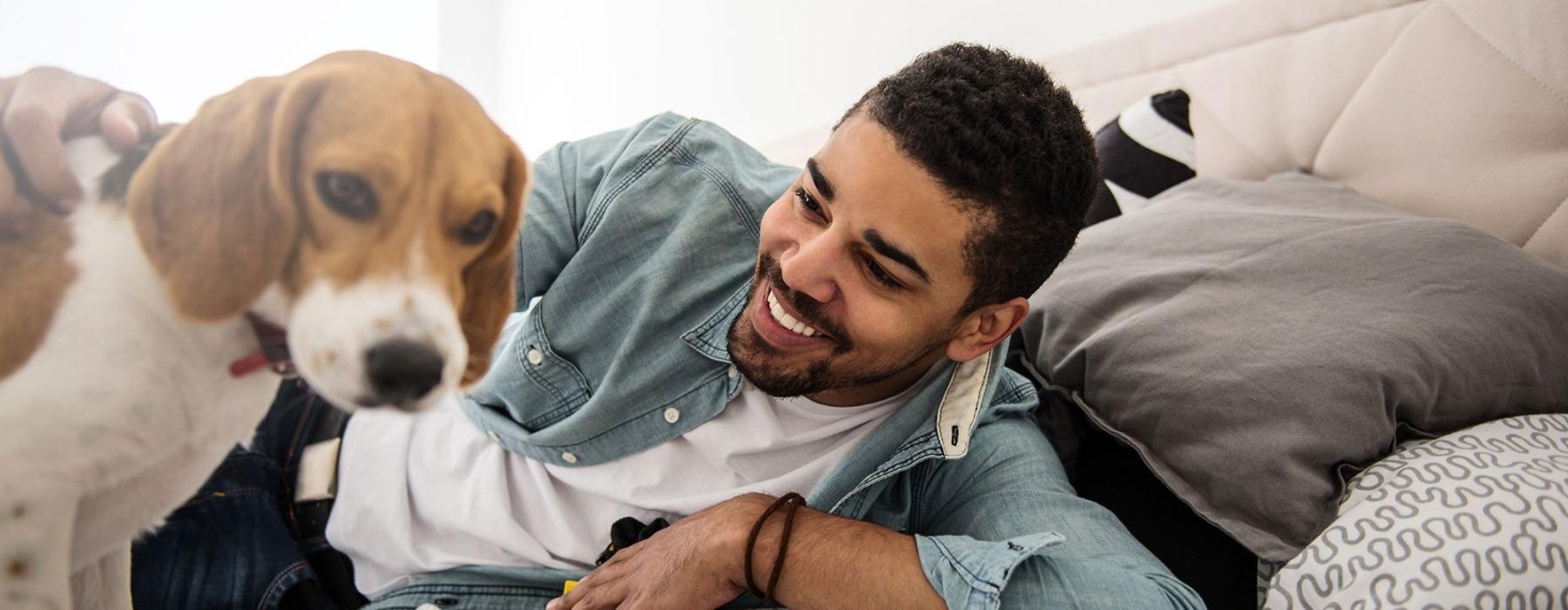 man smiles and pets his dog on a bed